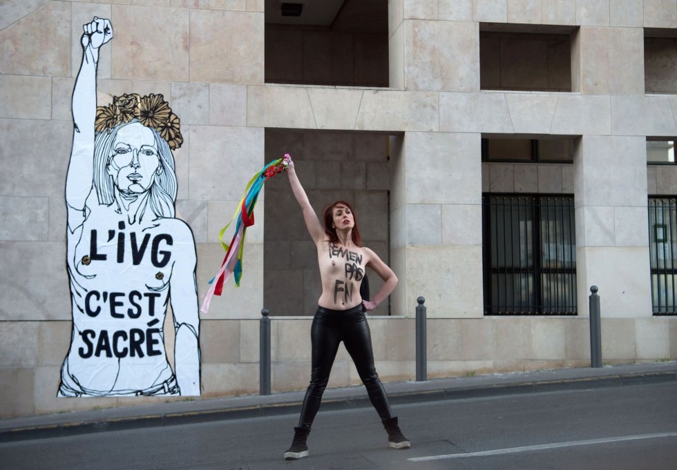 Una activista femenina con una inscripción pintada en su pecho, posa frente a una obra de arte con una inscripción que se traduce como IVG (Ley sobre el aborto voluntario) es sagrado en Marsella, Francia.