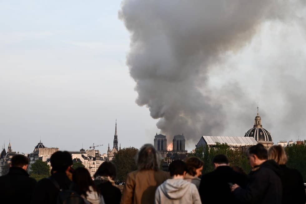Una gran cantidad de humo, visible en estos momentos desde kilómetros de distancia, sale del edificio. En la imagen, la gente observa cómo el humo y las llamas se elevan sobre las torres de la catedral.
